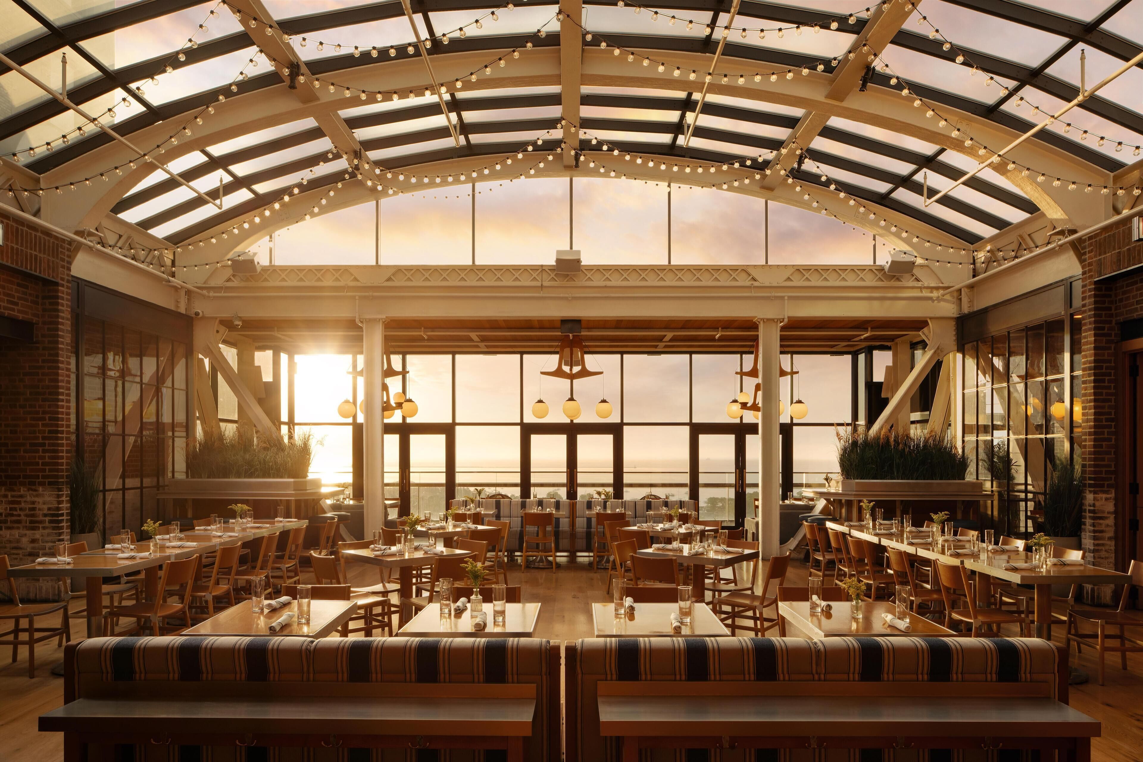 A spacious indoor dining area with high ceilings, large windows, and string lights.