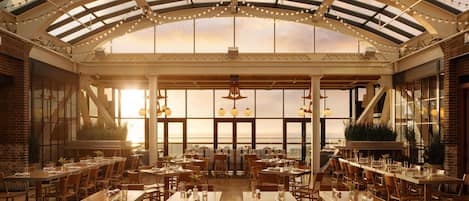 A spacious indoor dining area with high ceilings, large windows, and string lights.