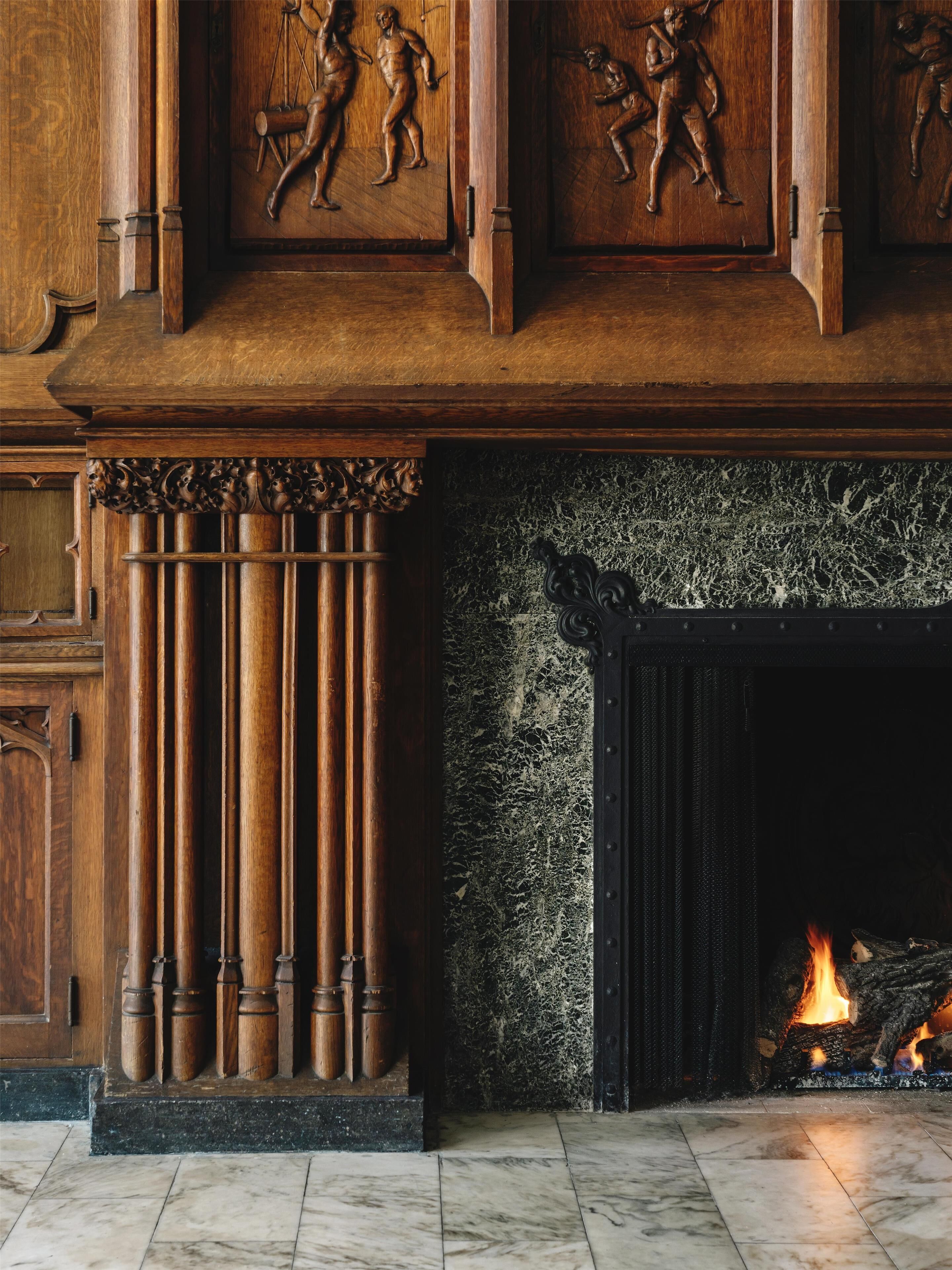 A fireplace with a fire, flanked by wooden columns and a marble floor.