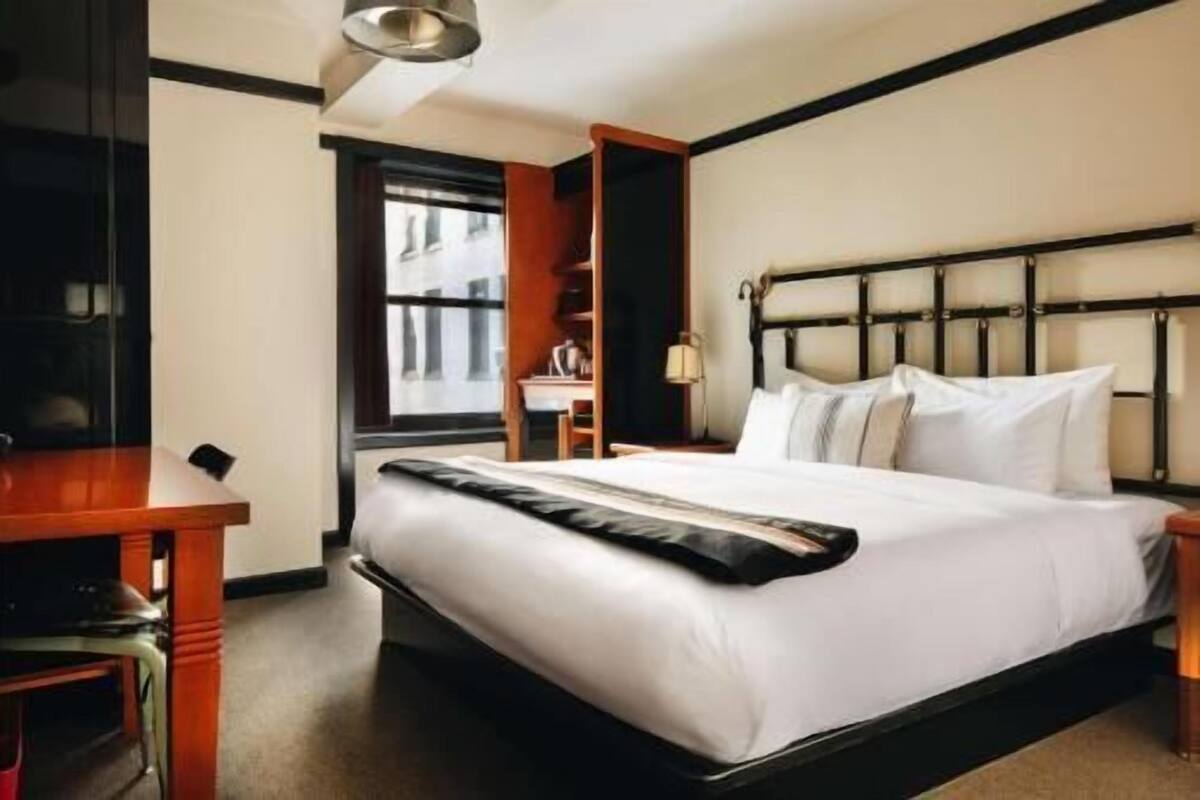 A hotel room with a bed, a desk, a chair, a window, and a nightstand.