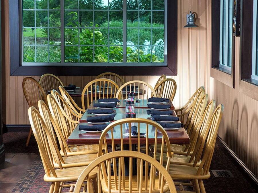 Un espace repas doté d’une grande fenêtre, de chaises en bois, d’une table rectangulaire et d’un sol recouvert d’une moquette.