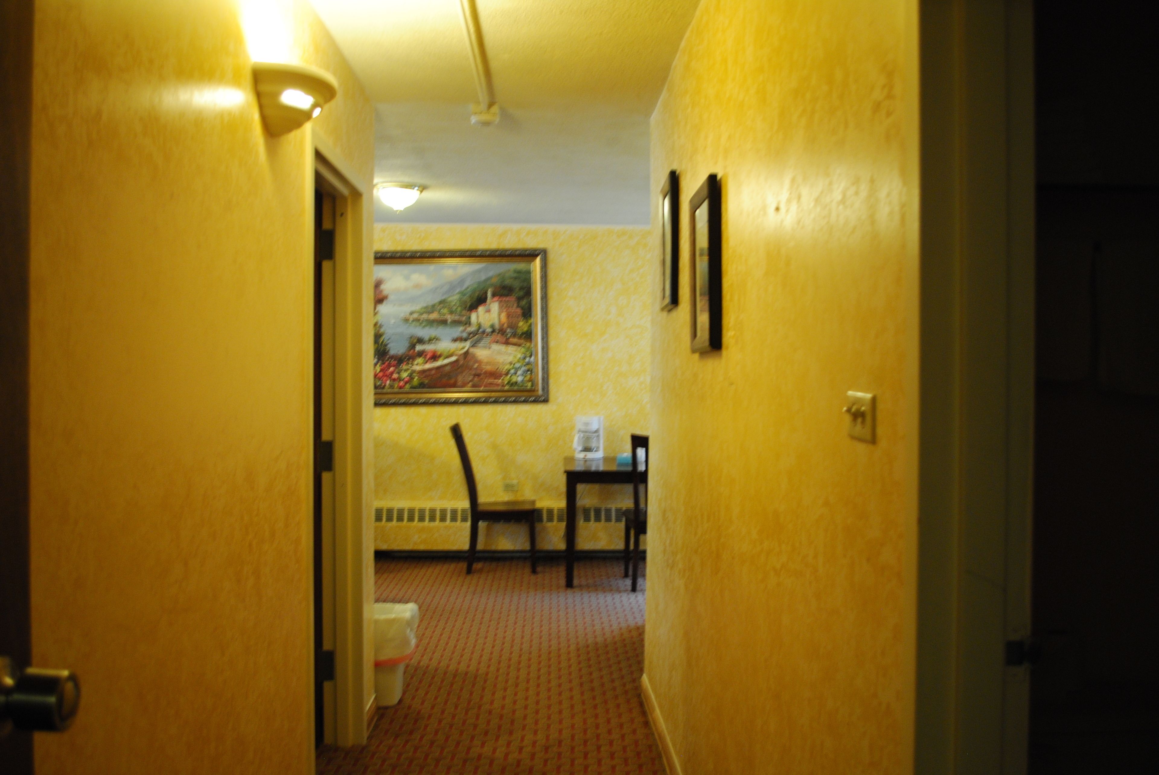 Un couloir aux murs jaunes, un tableau, une petite table avec une chaise et des toilettes.