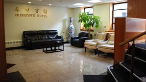 A hotel lobby with a black leather sofa, a white armchair, a large vase, and a potted plant. - Chinatown Hotel Chicago (Chicago)