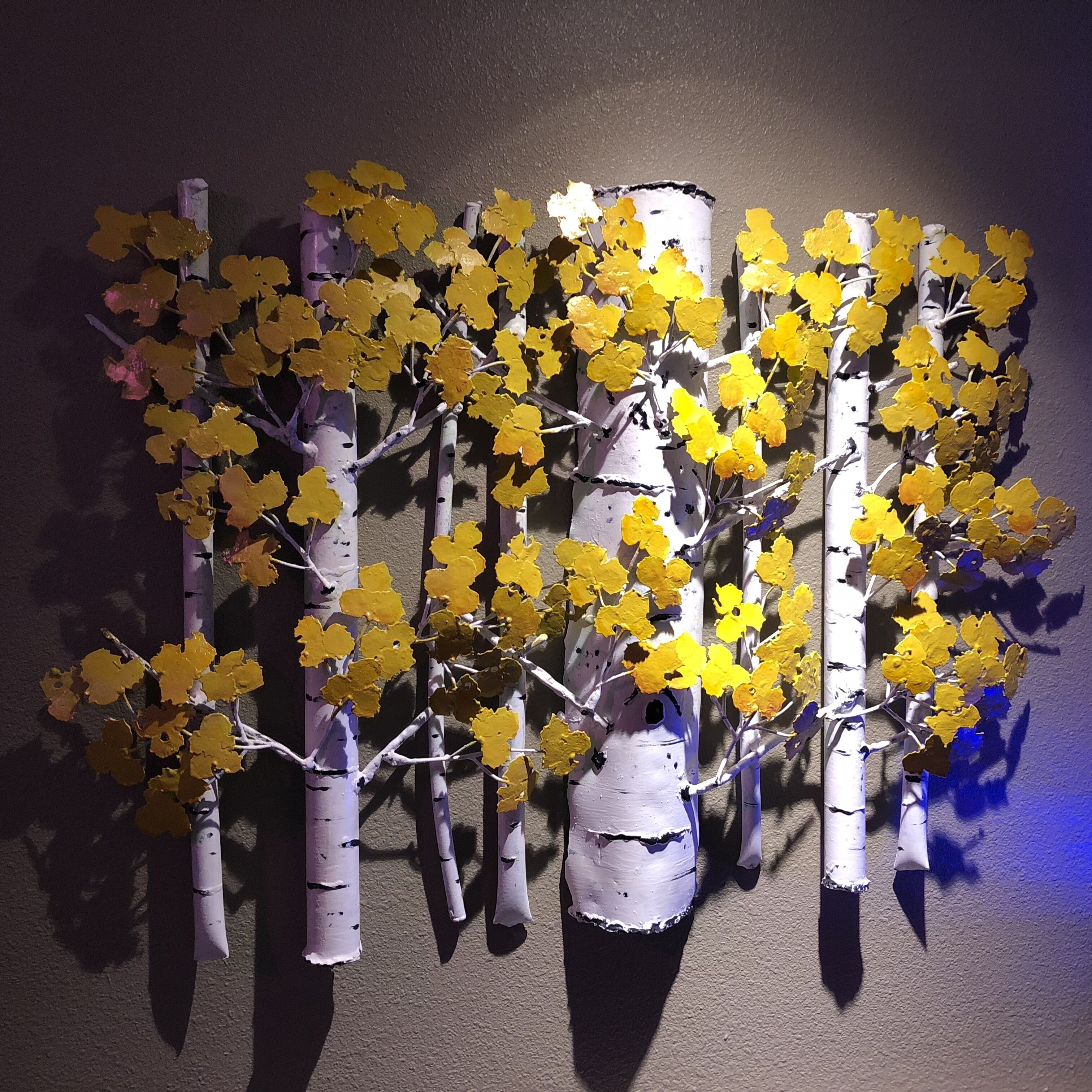 A wall-mounted decorative piece with stylized trees and yellow foliage.