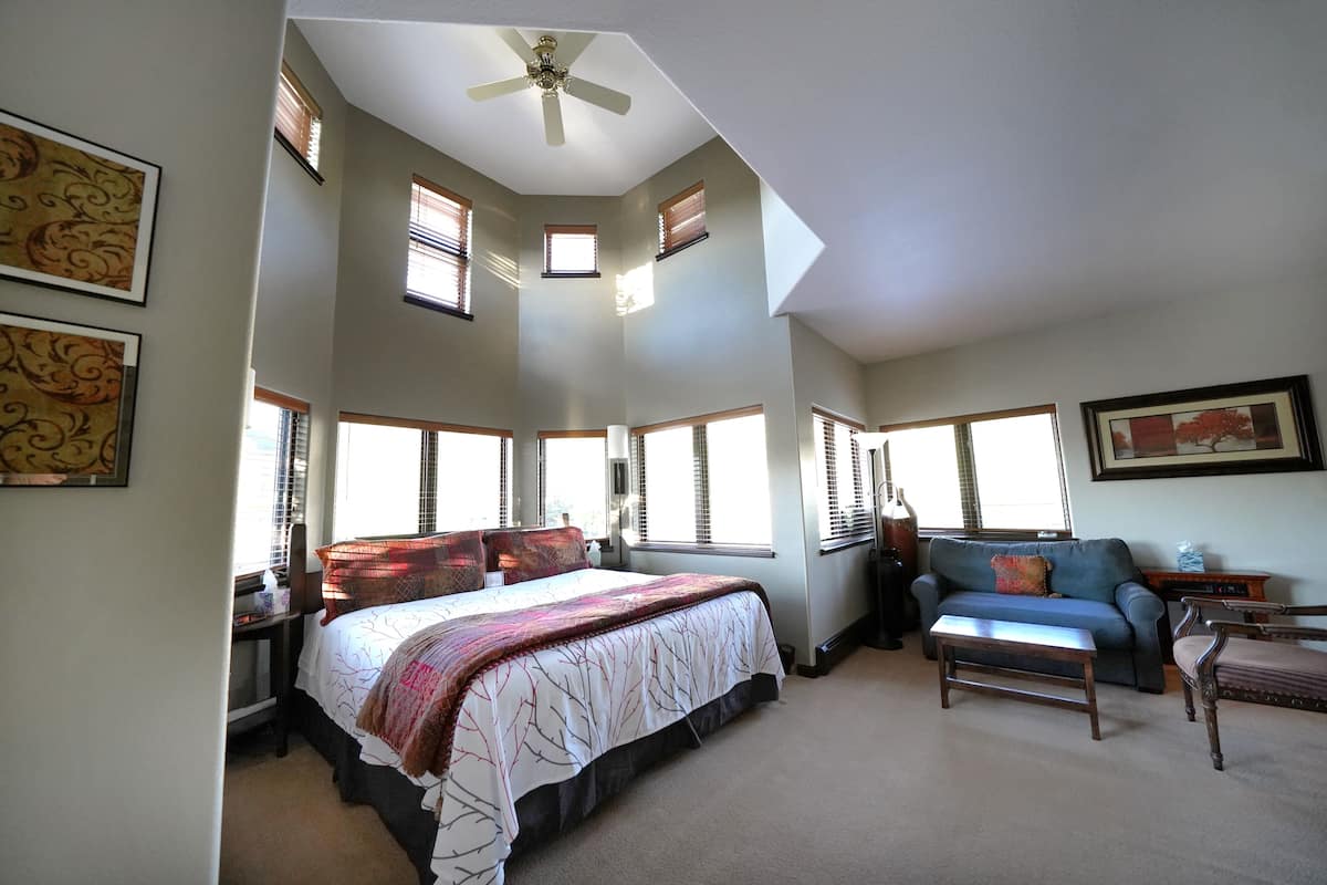 A bedroom with a bed, a desk, a chair, a sofa, and a ceiling fan.