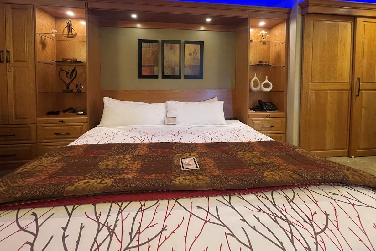 A bedroom with a large bed, wooden wardrobe, bedside tables, and wall-mounted artwork.