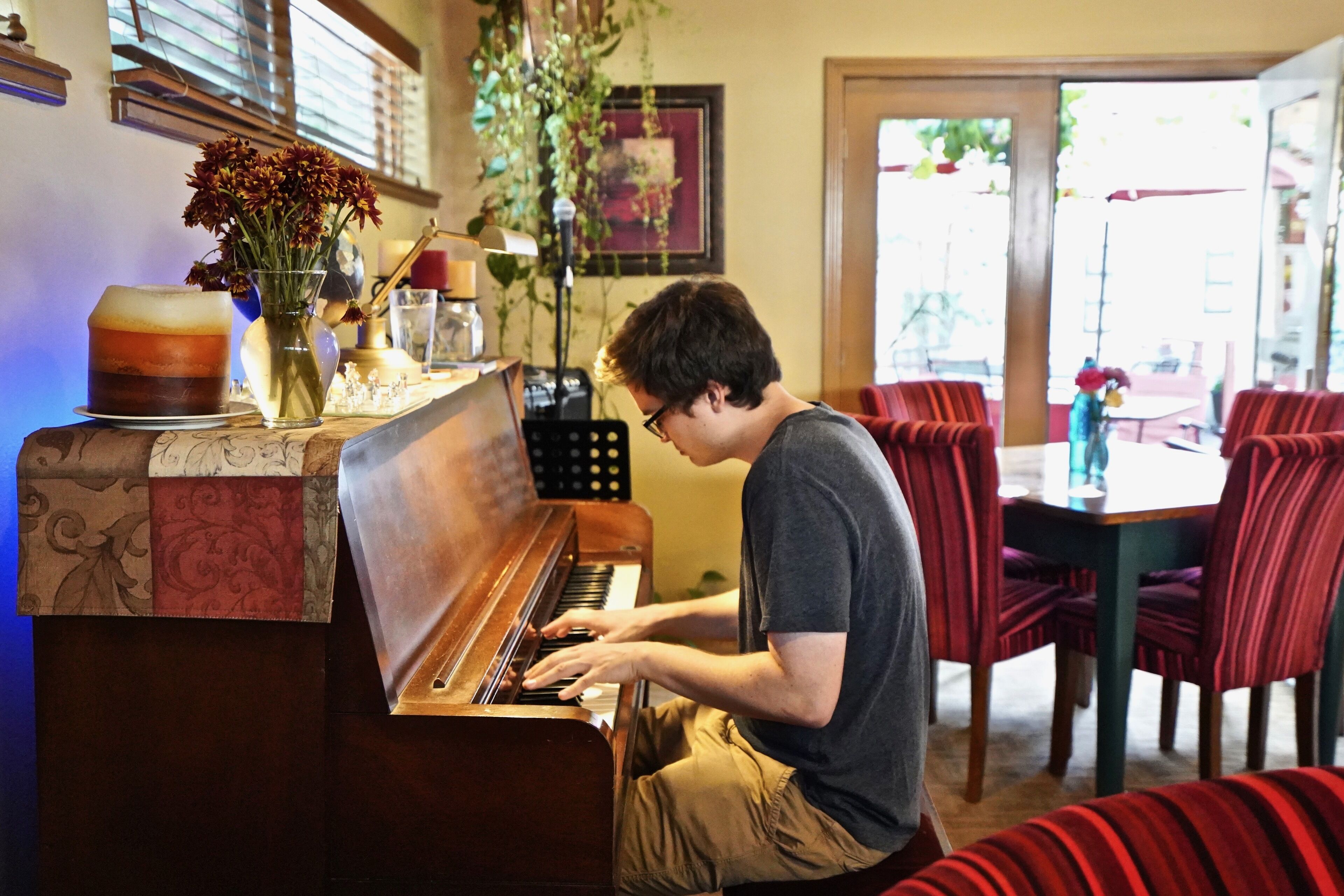 A person playing a piano in a room with a dining area in the background.