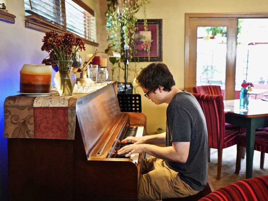 A person playing a piano in a room with a dining area in the background.