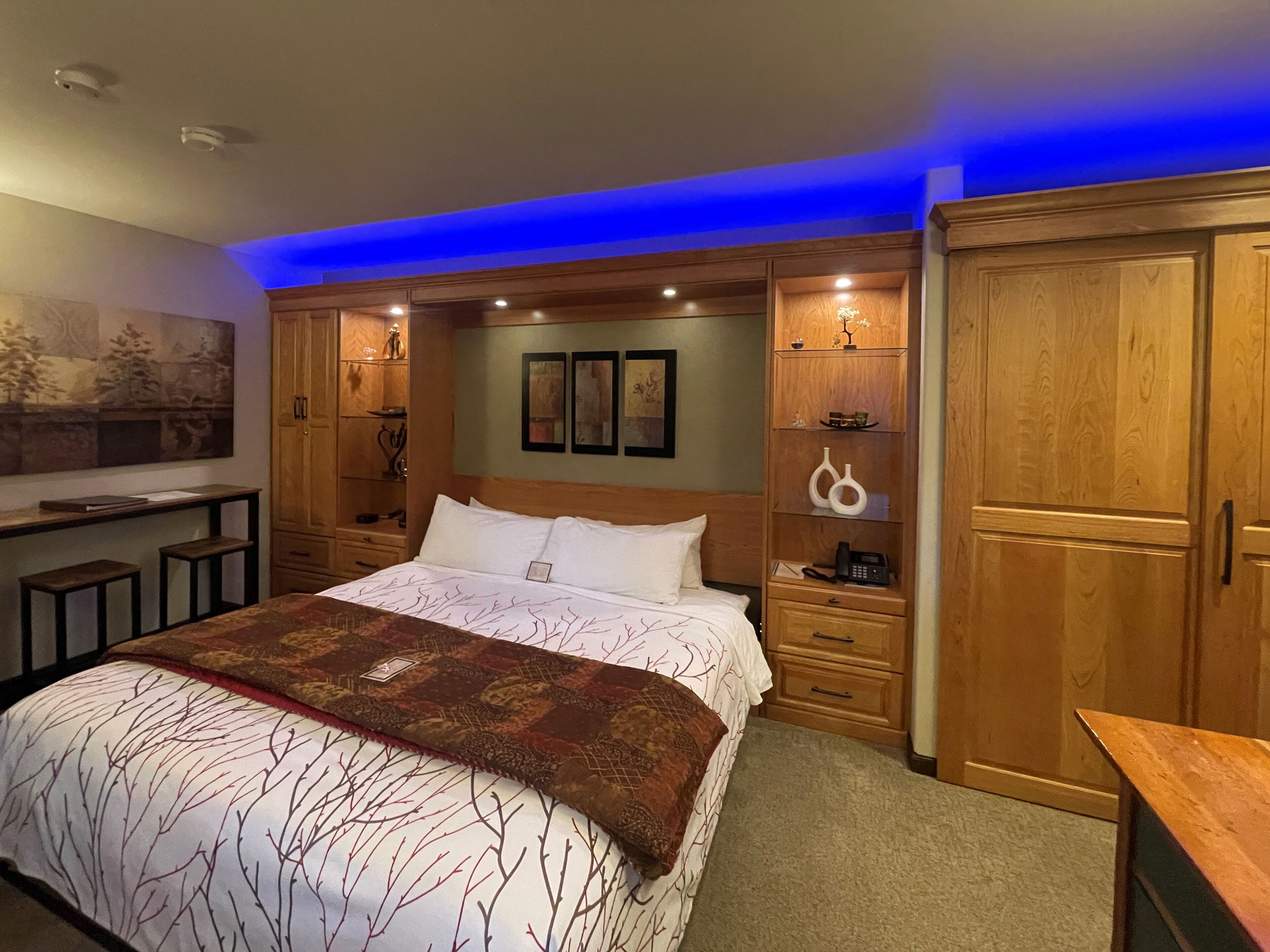 A bedroom with a large bed, wooden cabinets, a desk, and a painting on the wall.