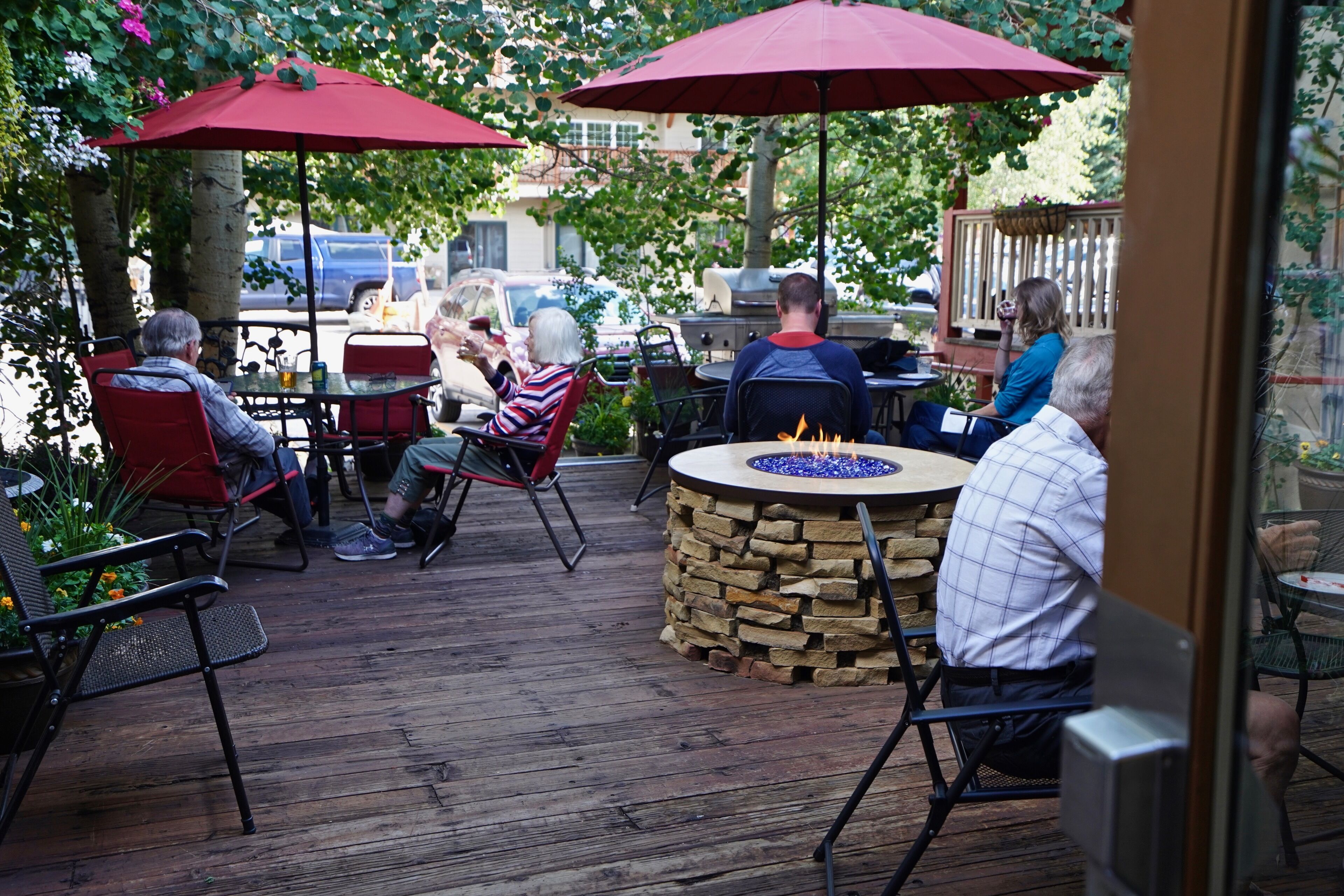 A wooden deck with outdoor seating, including red chairs and tables, and a stone fire pit.