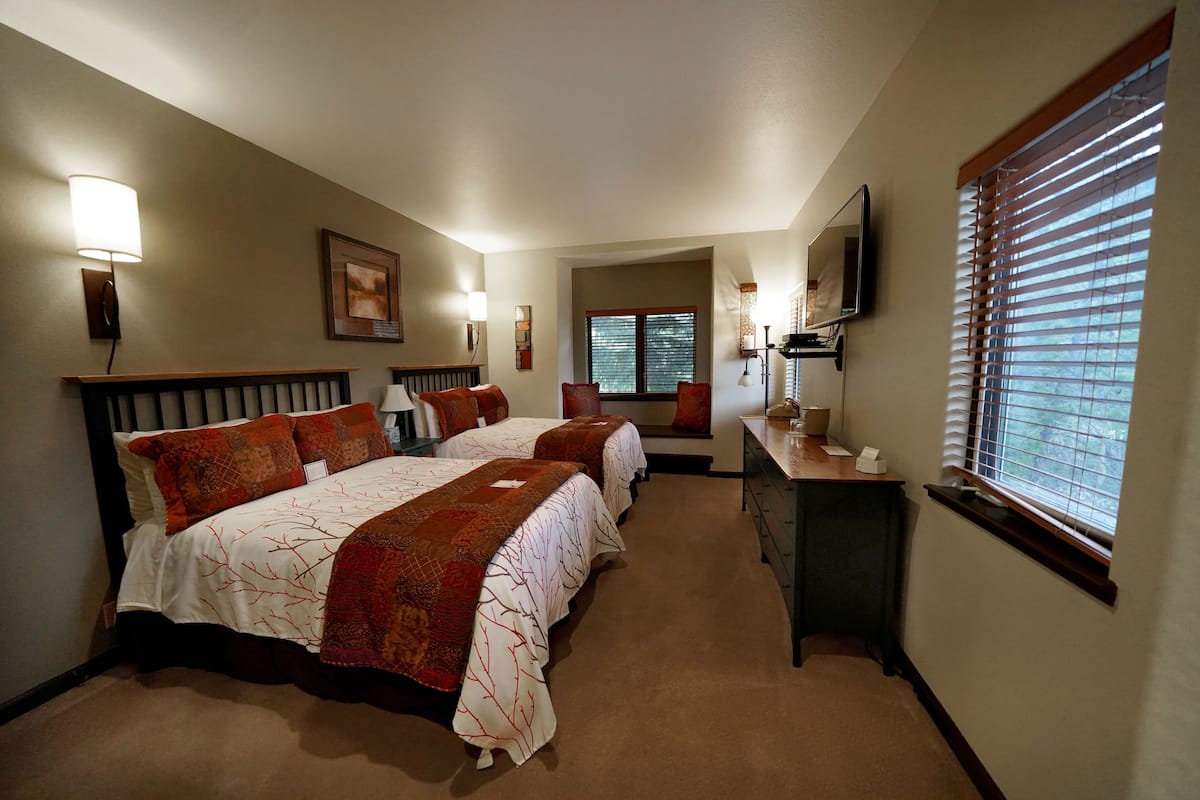 A hotel room with two beds, a desk, a chair, a TV, and a window with blinds.
