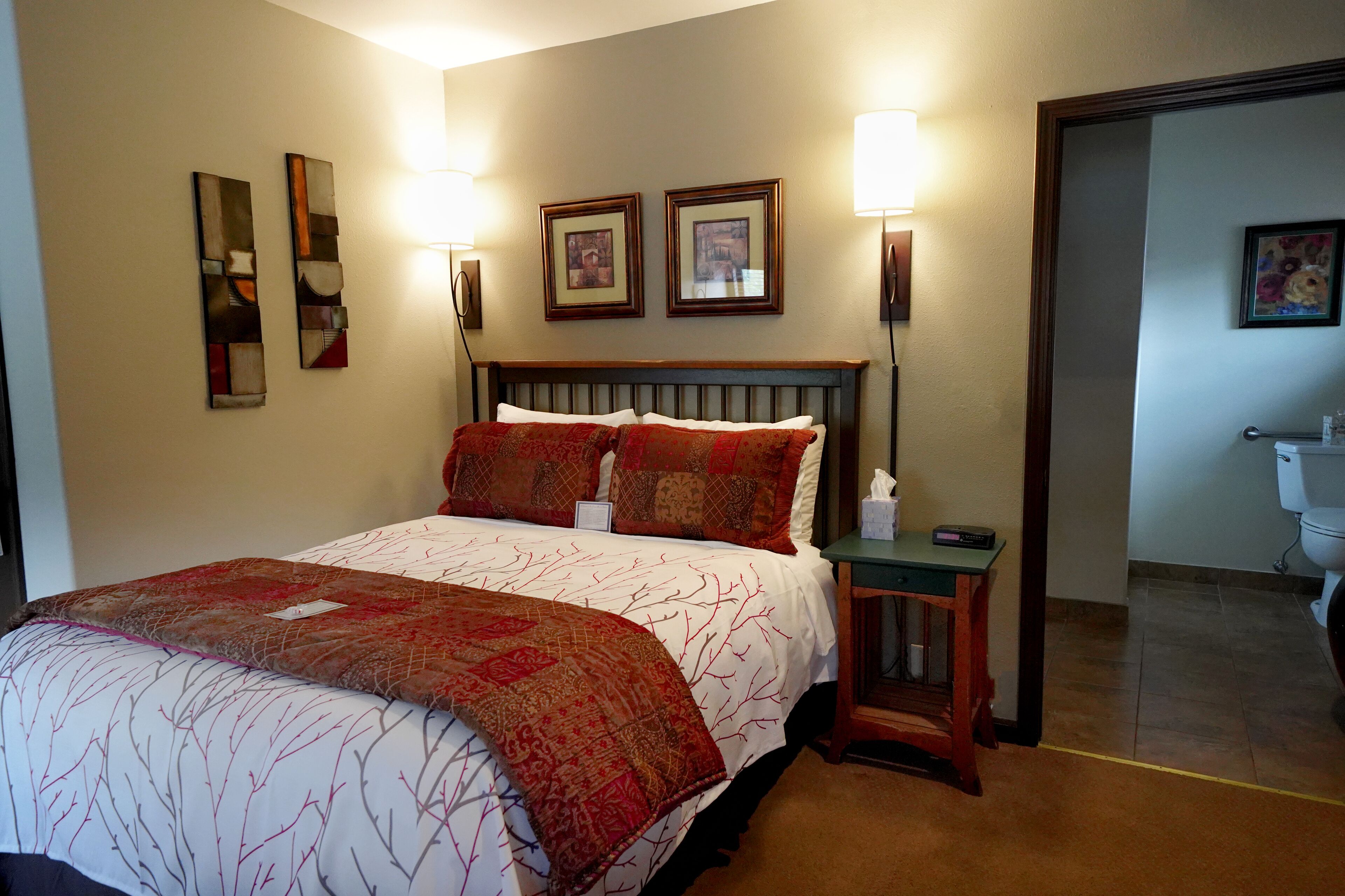A hotel room with a bed, two framed pictures on the wall, a nightstand, and a bathroom visible through an open door.