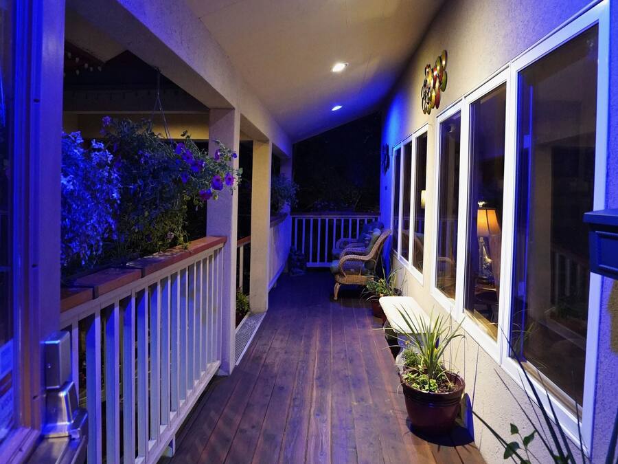 A covered outdoor area with wooden flooring, potted plants, and seating.