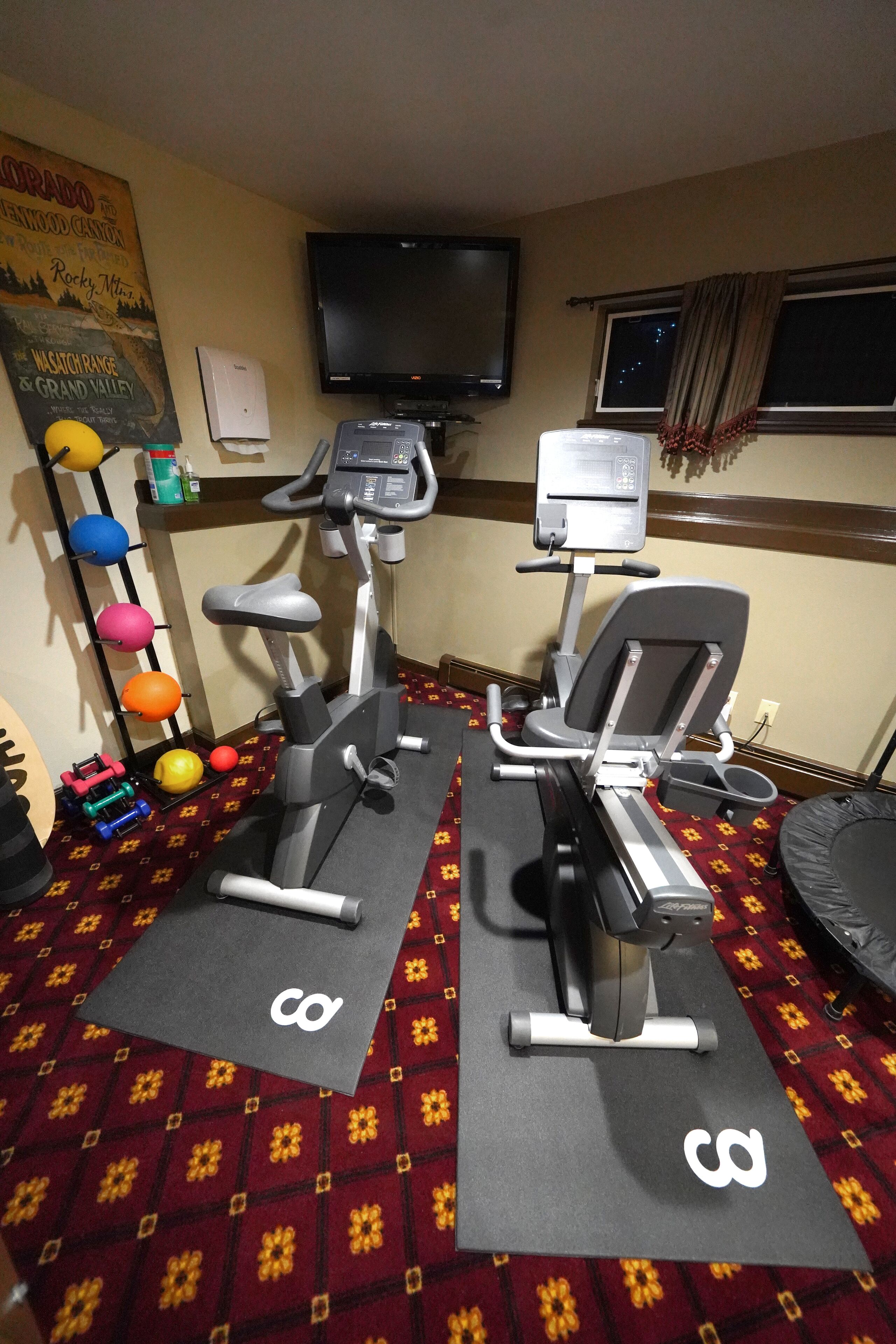 A gym with two treadmills, a wall-mounted TV, and a poster on the wall.