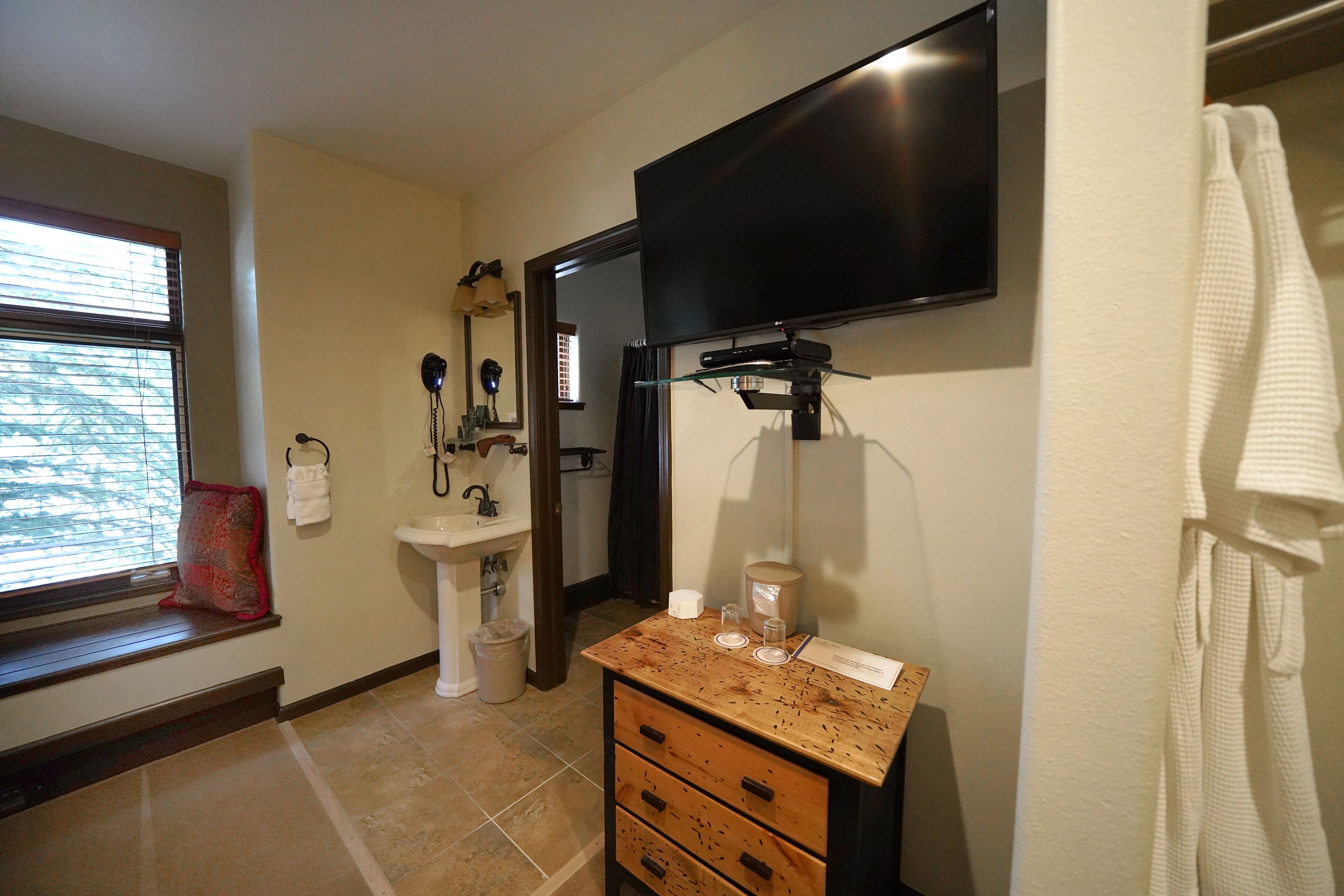 A bathroom with a vanity, sink, mirror, and a television mounted above the mirror.