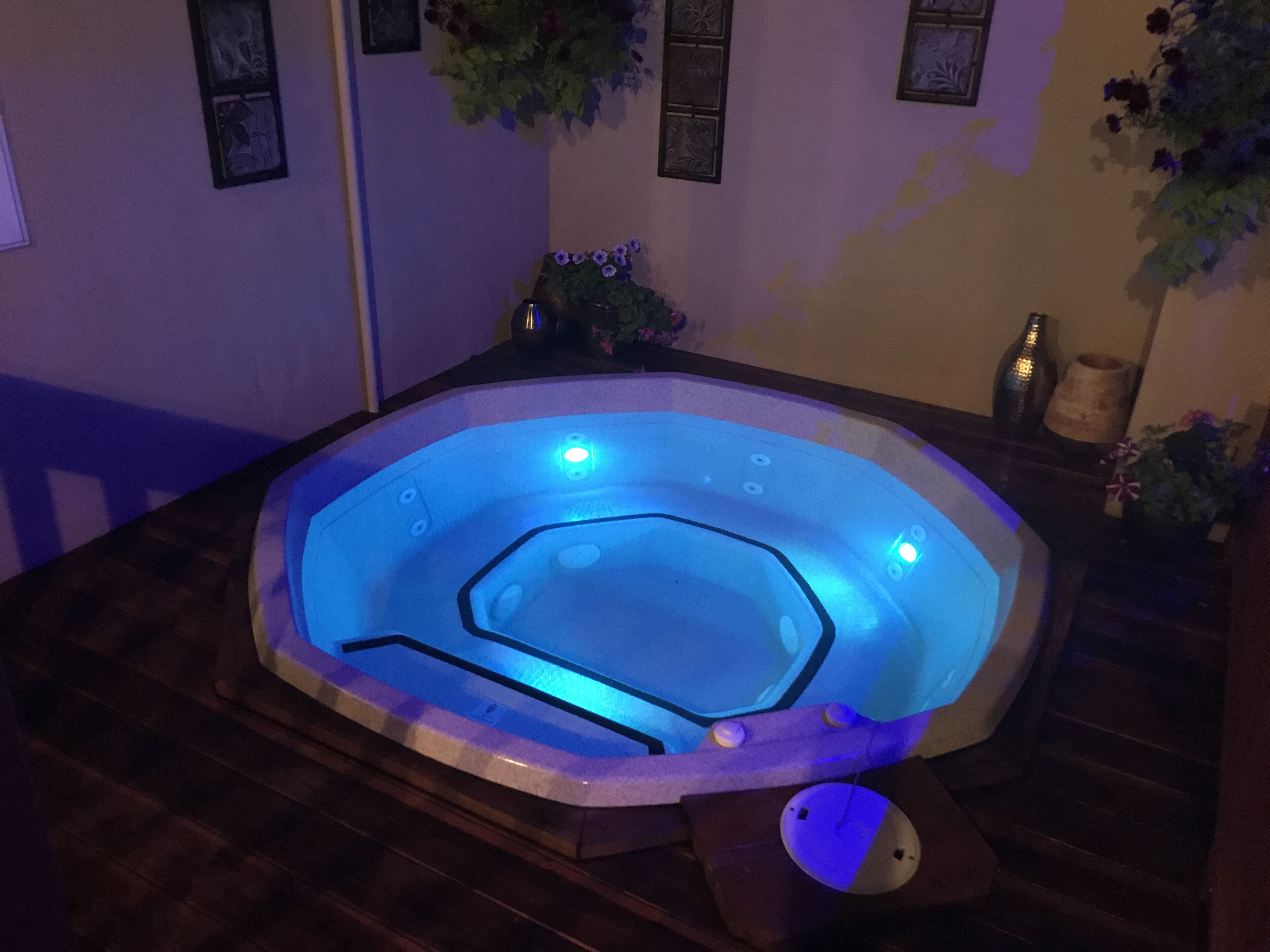 Un bain à remous avec un éclairage bleu, un revêtement de sol en bois et des décorations murales.