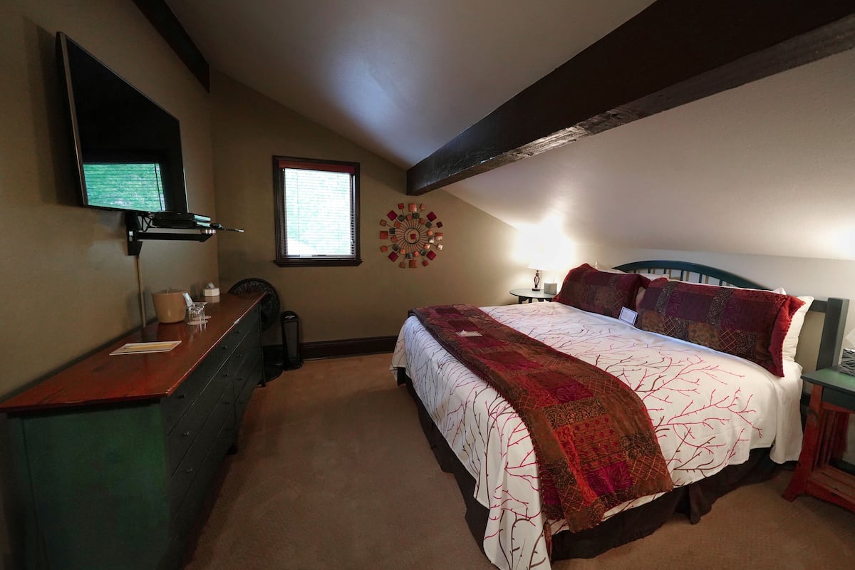 A bedroom with a bed, a desk, a chair, a window, and a wall-mounted TV.