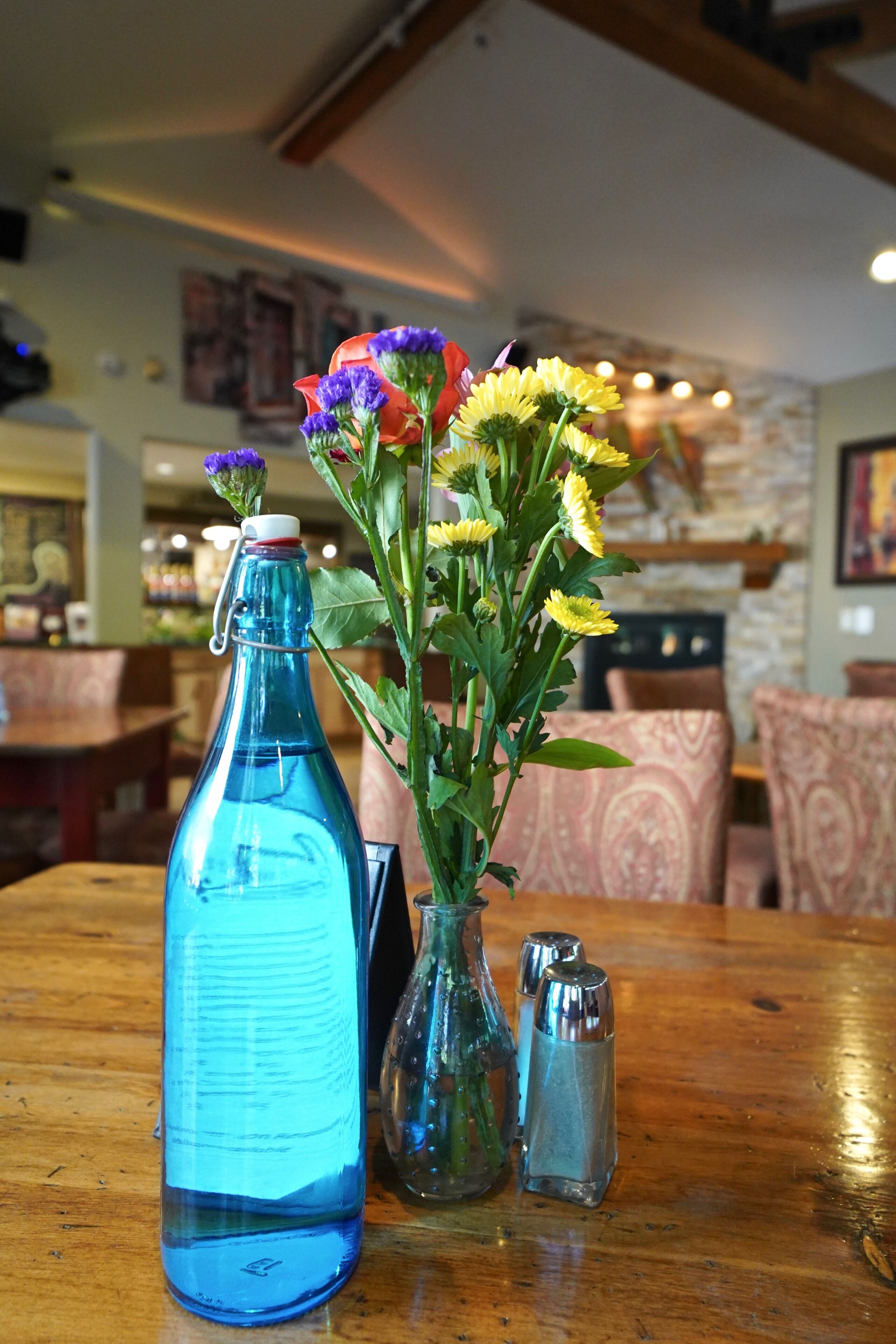 A table with a blue bottle, a clear vase with flowers, and two salt shakers.