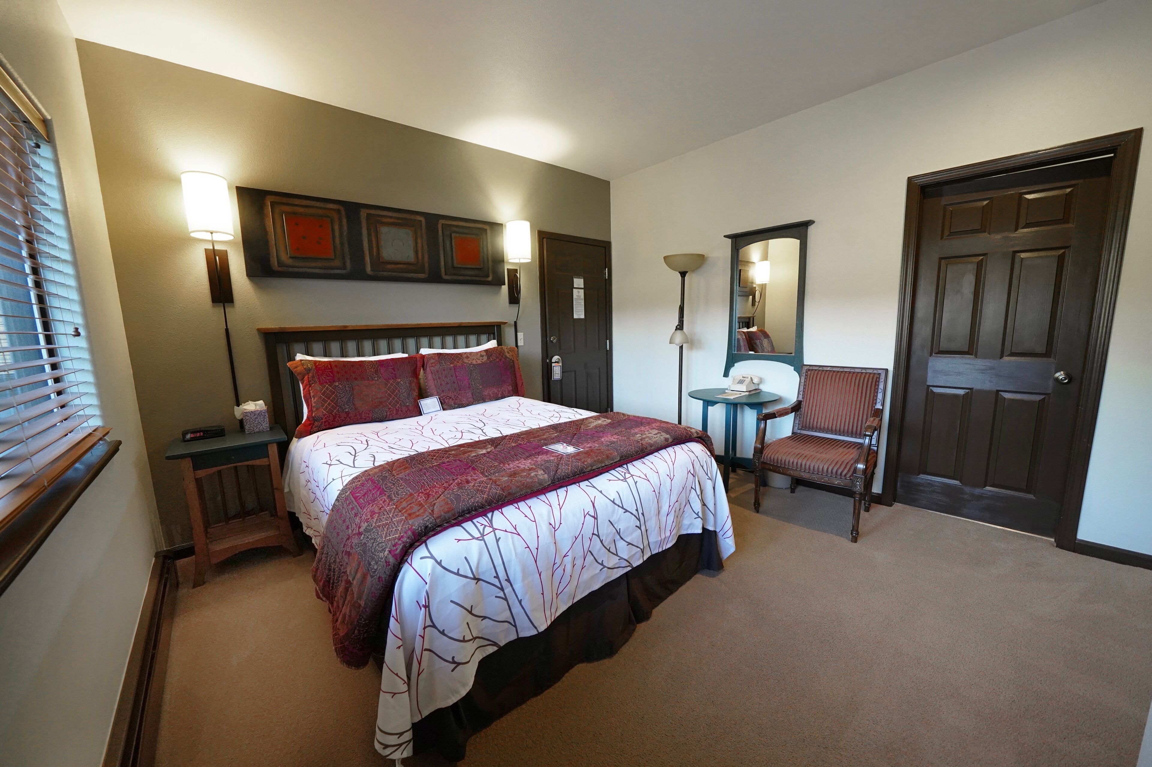 Habitación de hotel con una cama grande, mesitas de noche, una silla, un escritorio y una puerta.