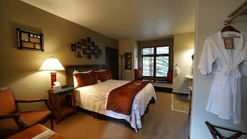 A hotel room with a bed, a chair, a desk, a lamp, a robe, and a window.