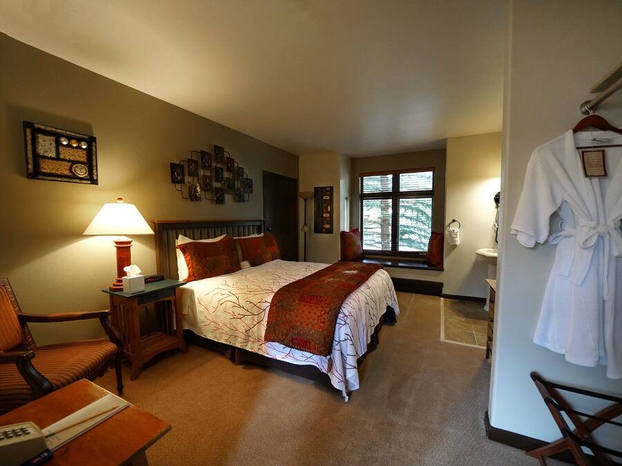 A hotel room with a bed, a chair, a desk, a lamp, a robe, and a window.