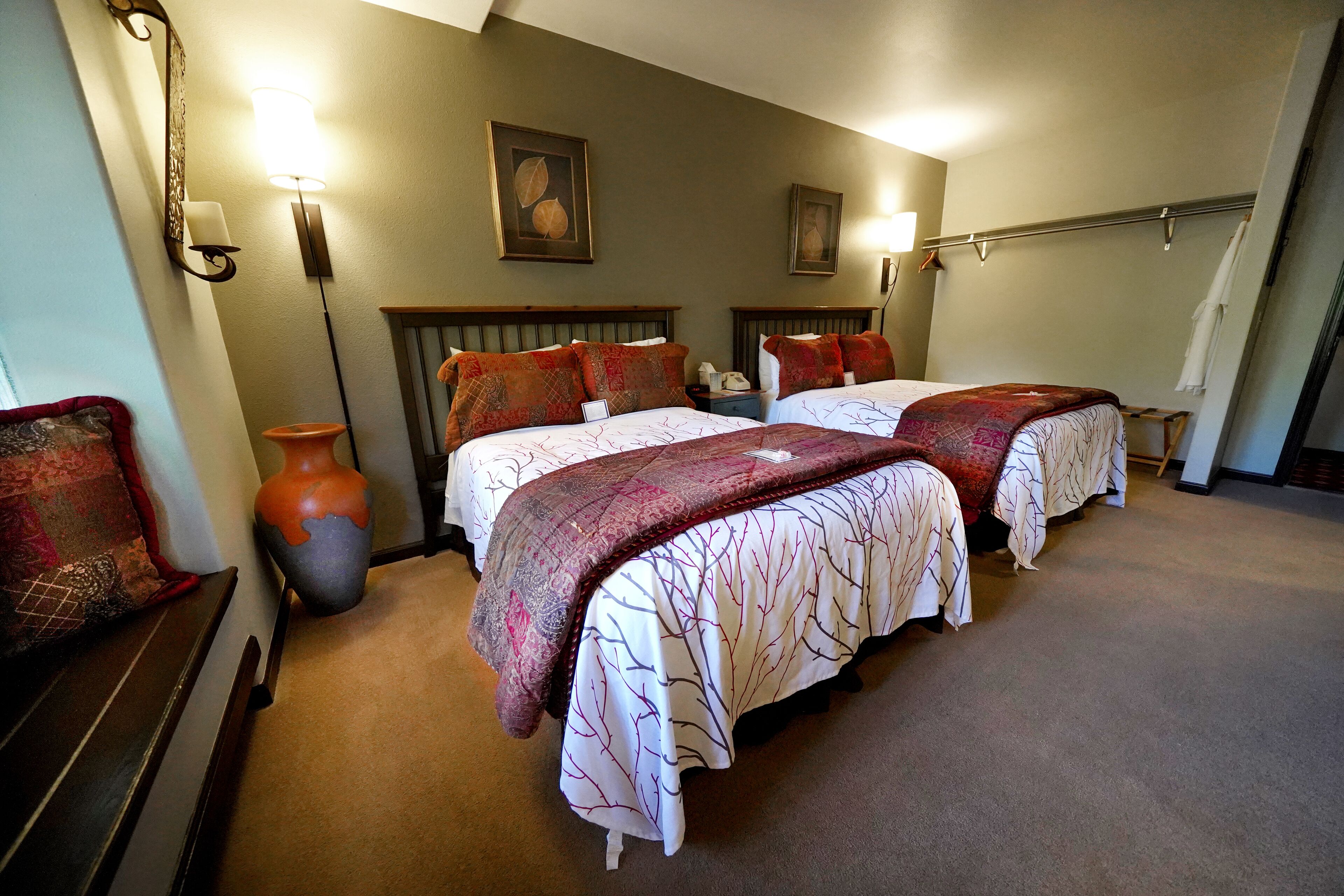 A hotel room with two beds, a vase, and wall-mounted lamps.