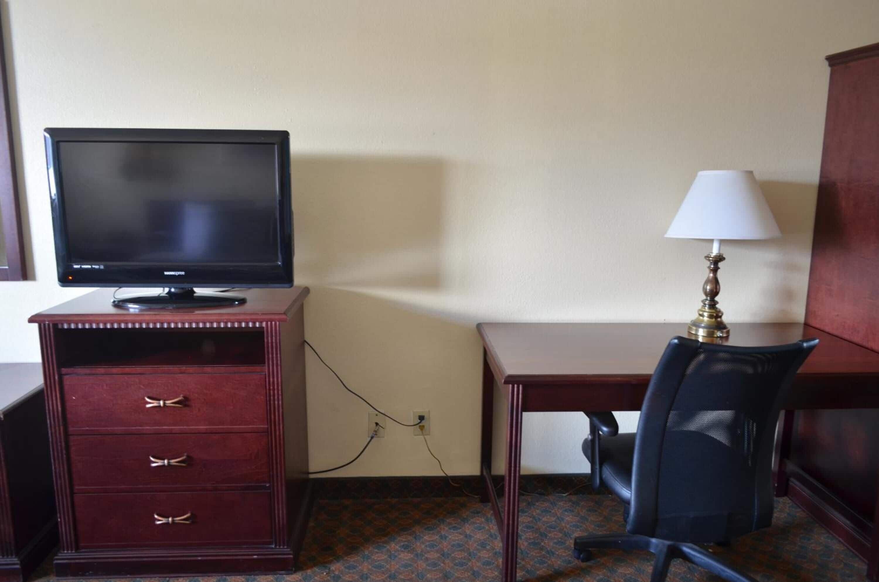 Una habitación de hotel con escritorio, una silla, televisor y lámpara.