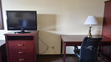 Una habitación de hotel con escritorio, una silla, televisor y lámpara.