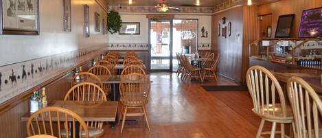 A restaurant interior with wooden flooring, wooden chairs, tables, ceiling fans, framed pictures on the walls, and a visible restroom sign.