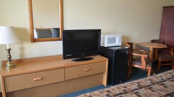 Une chambre d’hôtel comprenant un lit, une commode en bois avec des tiroirs, une télévision, un four à micro-ondes, un petit réfrigérateur, une lampe et une table ronde avec deux chaises.
