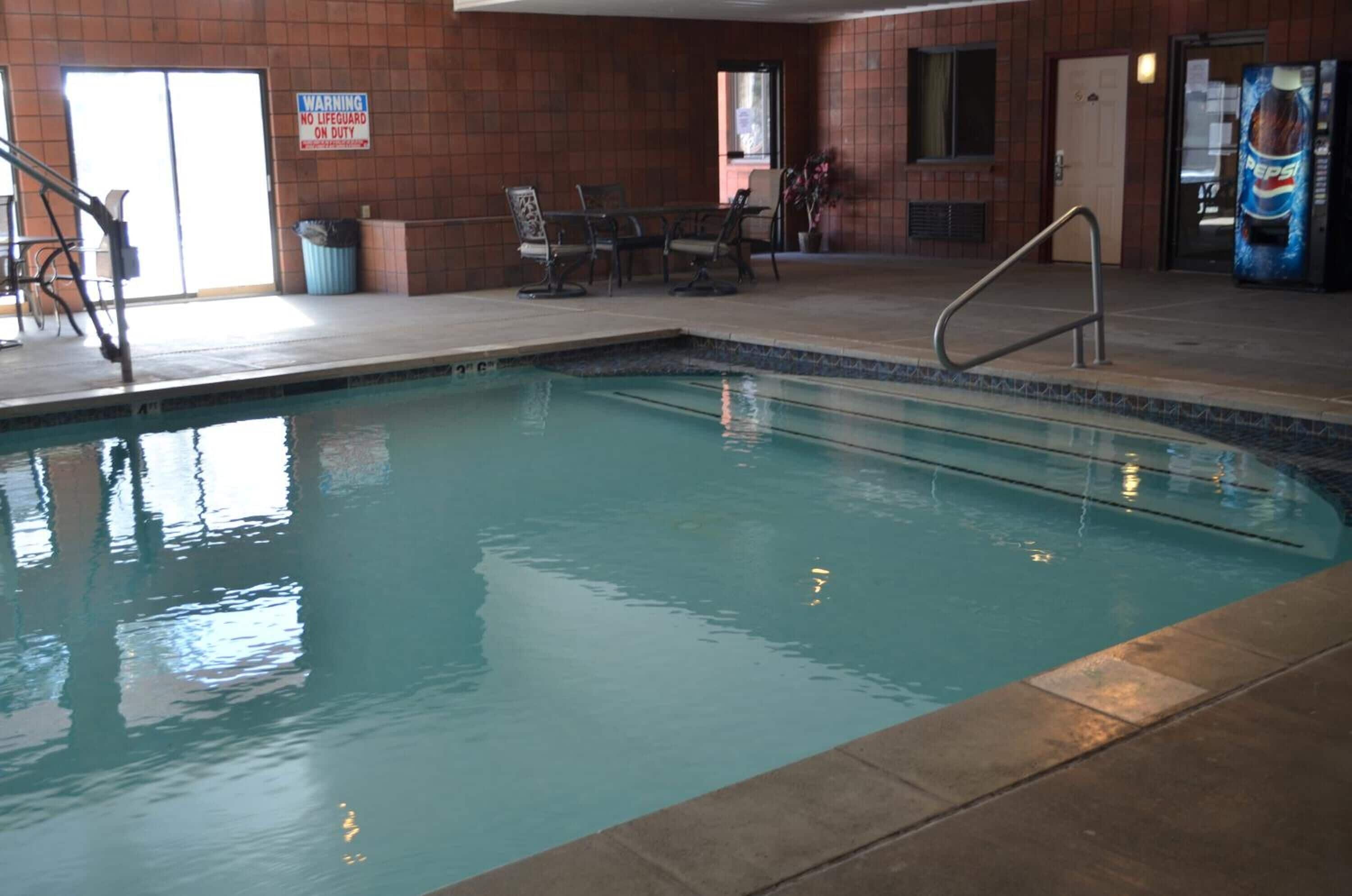 An indoor swimming pool with a lifeguard sign, a seating area, and a vending machine.