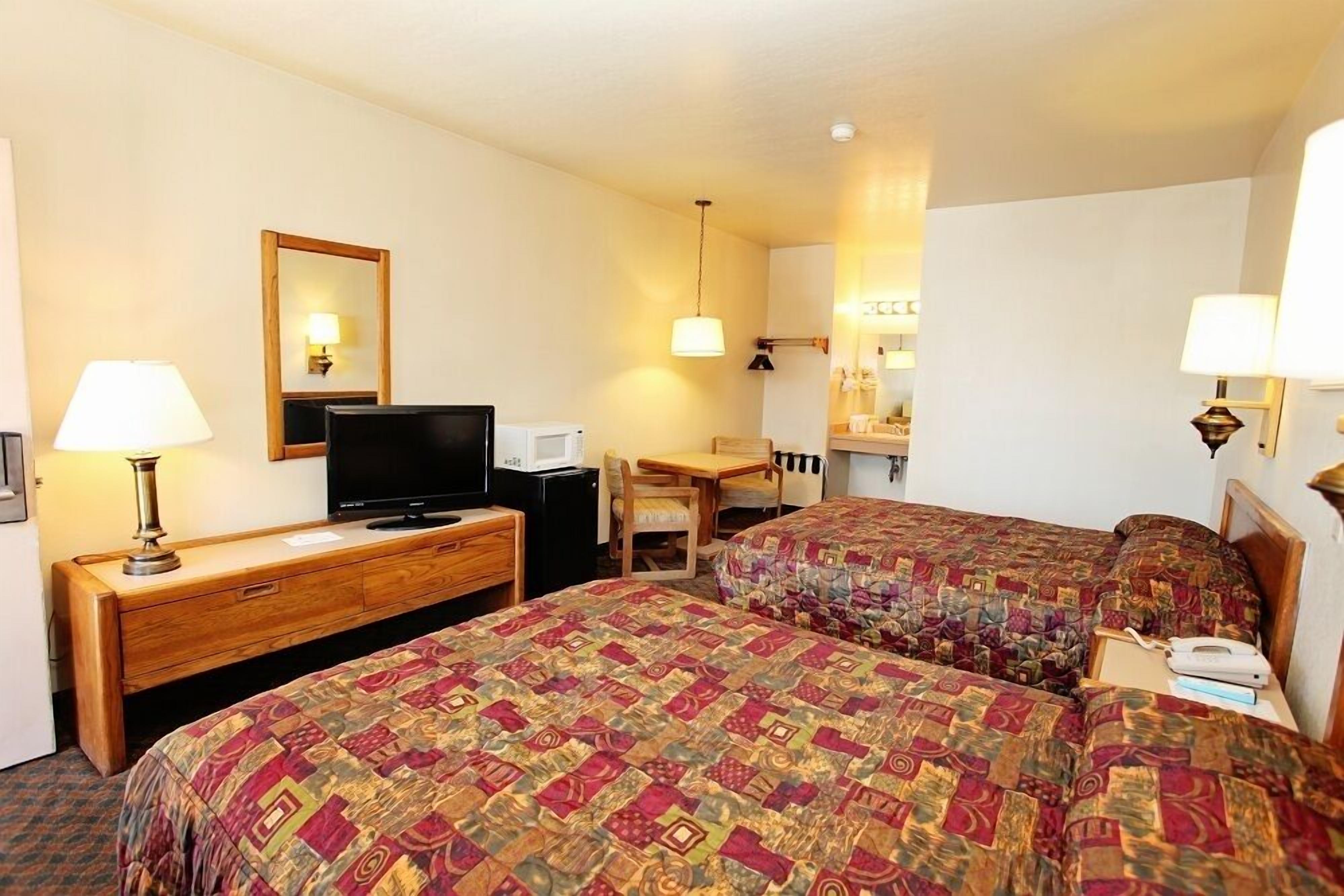 A hotel room with two beds, a desk, a television, and a mirror.