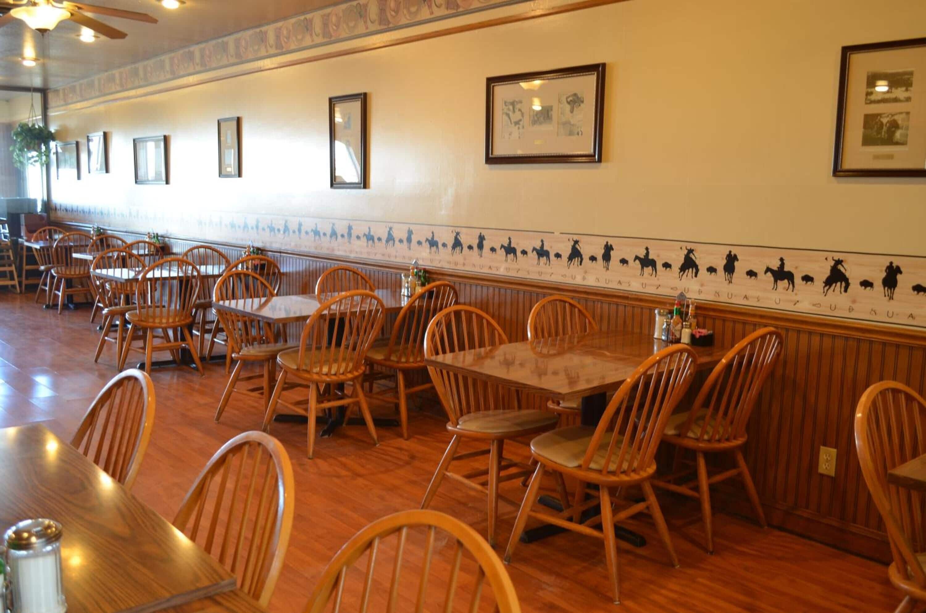 A restaurant with wooden tables and chairs, framed pictures on the walls, and a patterned border along the wall.