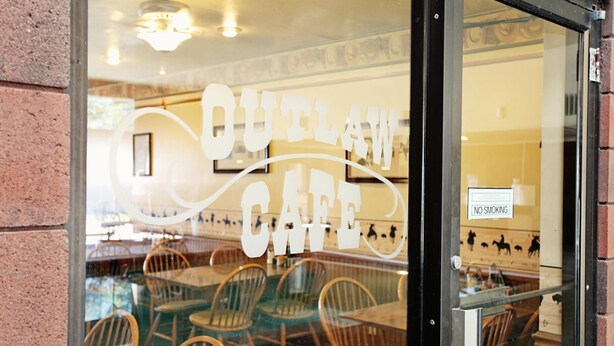 A restaurant with a 'Cowboy Cafe' sign on the window, wooden chairs, and a 'No Smoking' sign inside. - National 9 Inn Wellington (Wellington)