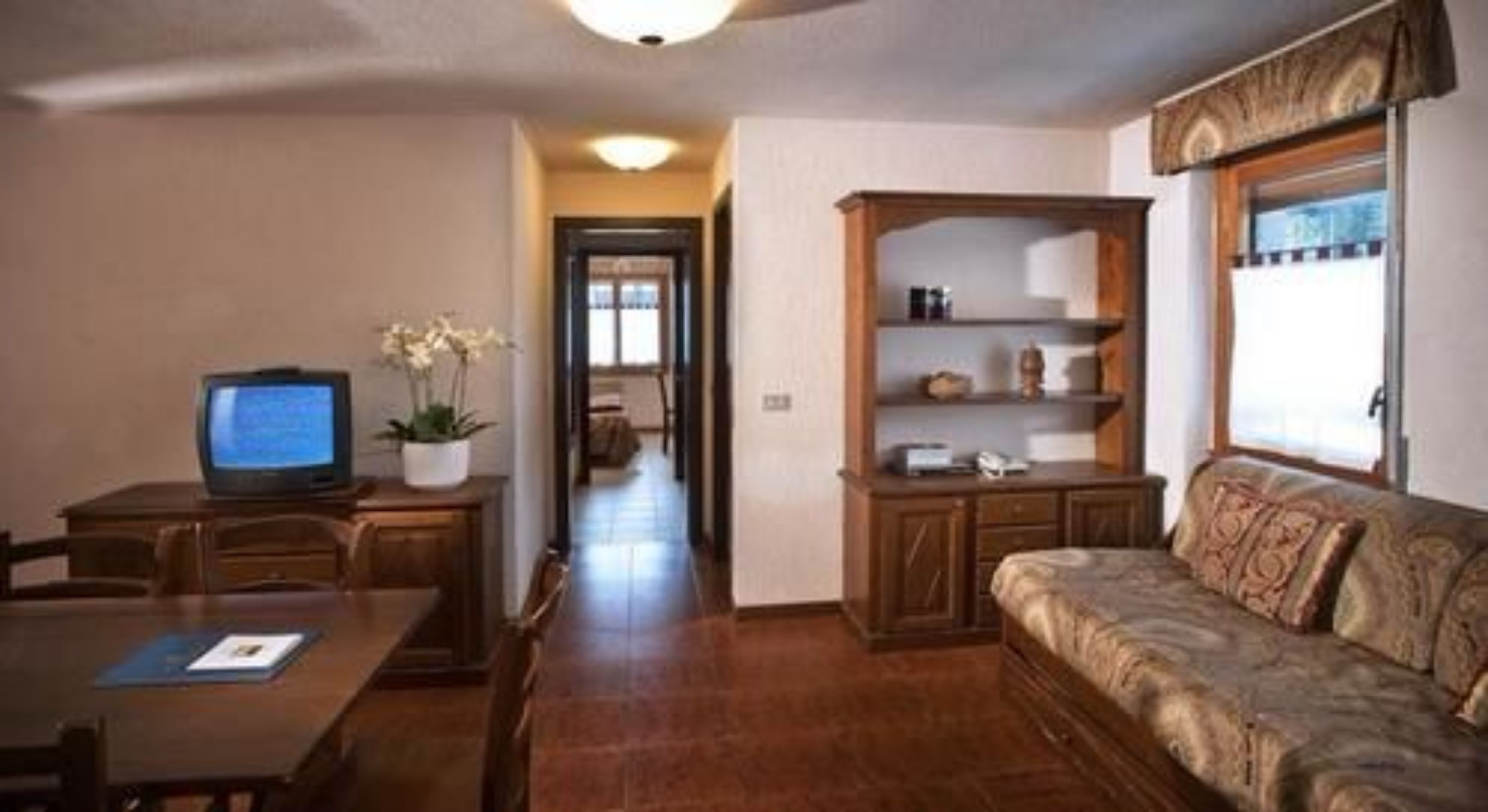 Una sala de estar con televisión, un sofá, un aparador de madera y un pasillo que conduce a otra habitación.