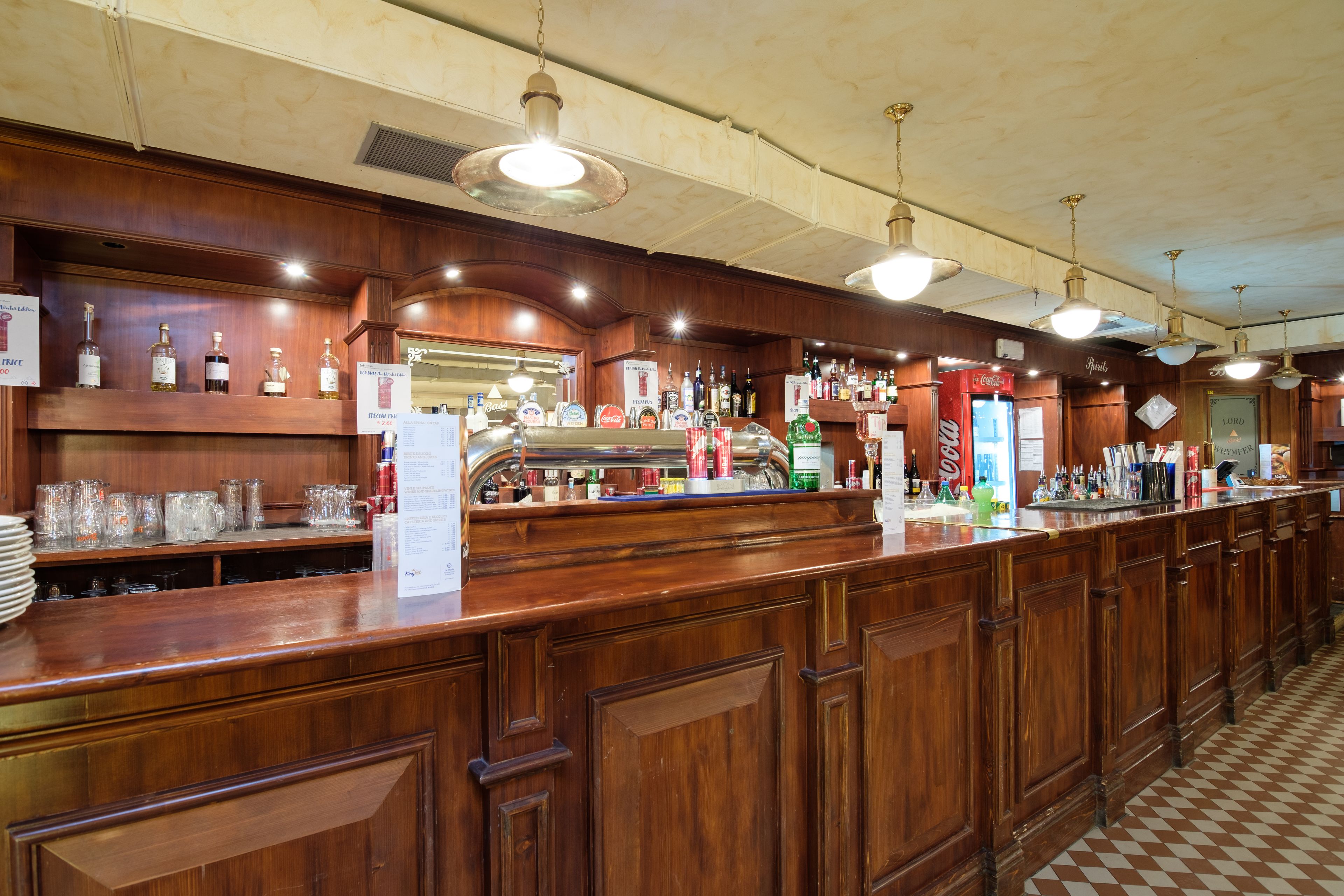 Eine Bar mit Holzwandverkleidung, hängenden Lampen und einer Auswahl an Flaschen und Gläsern auf Regalen.