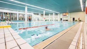 An indoor swimming pool with lanes, a lifeguard, and a staircase leading to an upper level.