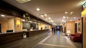 A hotel reception area with a reception desk, a TV screen, and a red couch.