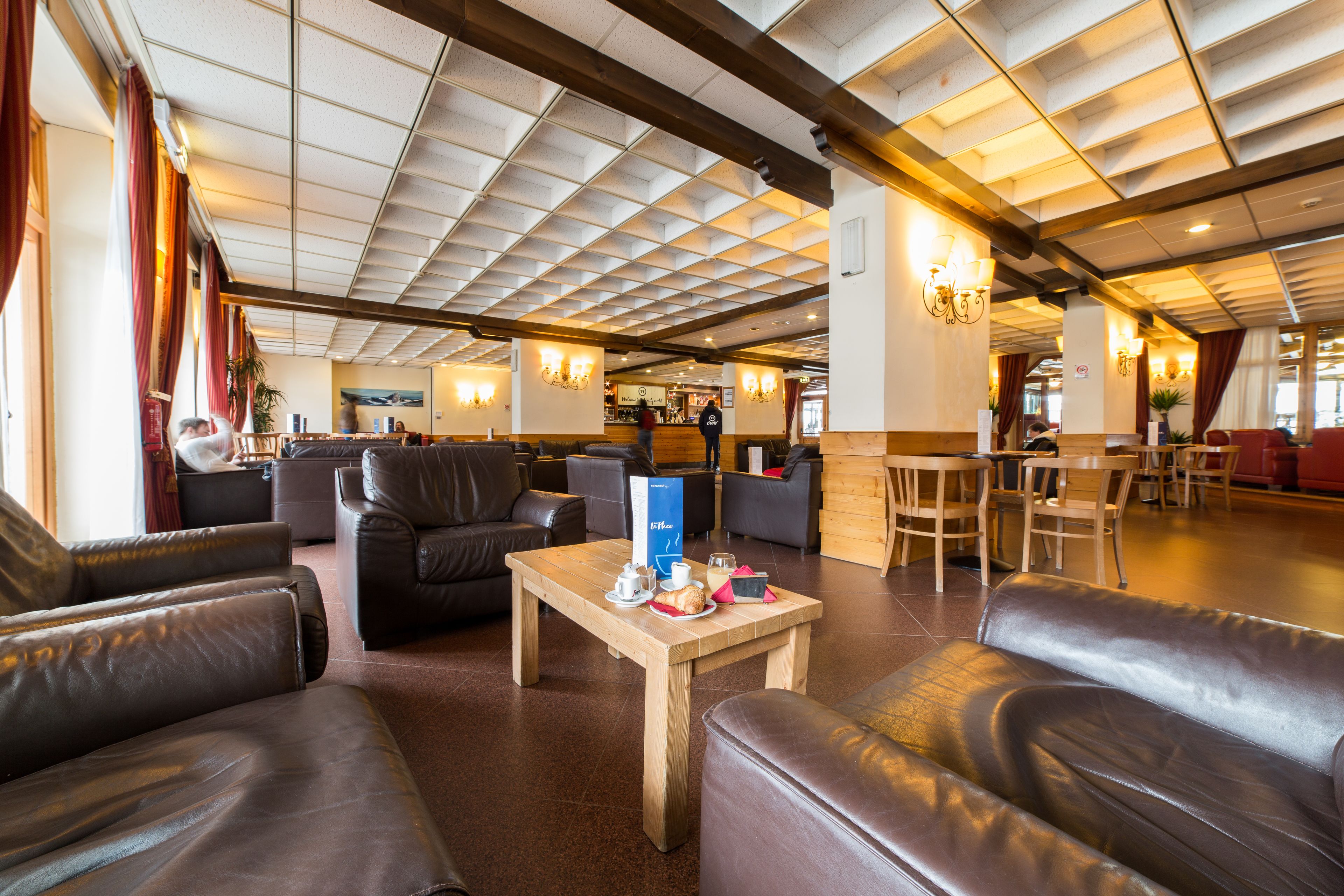 A spacious lobby with leather sofas, a wooden coffee table, and a high ceiling with exposed beams.