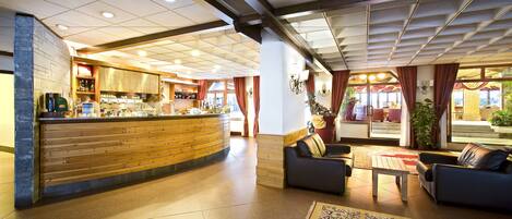 A hotel lobby with a reception desk, seating area, and a view of the outdoor terrace.