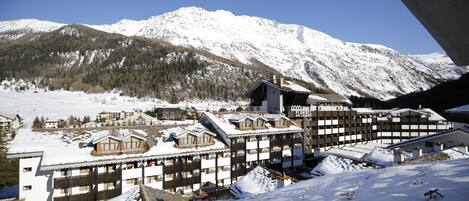 Un complejo turístico en la montaña cubierto de nieve, con edificios de estilo chalet, pistas de esquí y un cielo azul despejado.