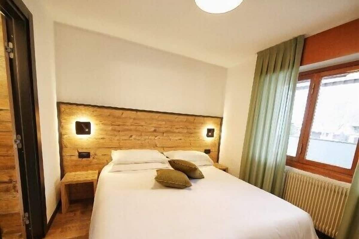 Habitación de hotel con una cama grande, cabecera de madera, lámparas de noche y una ventana con cortinas.