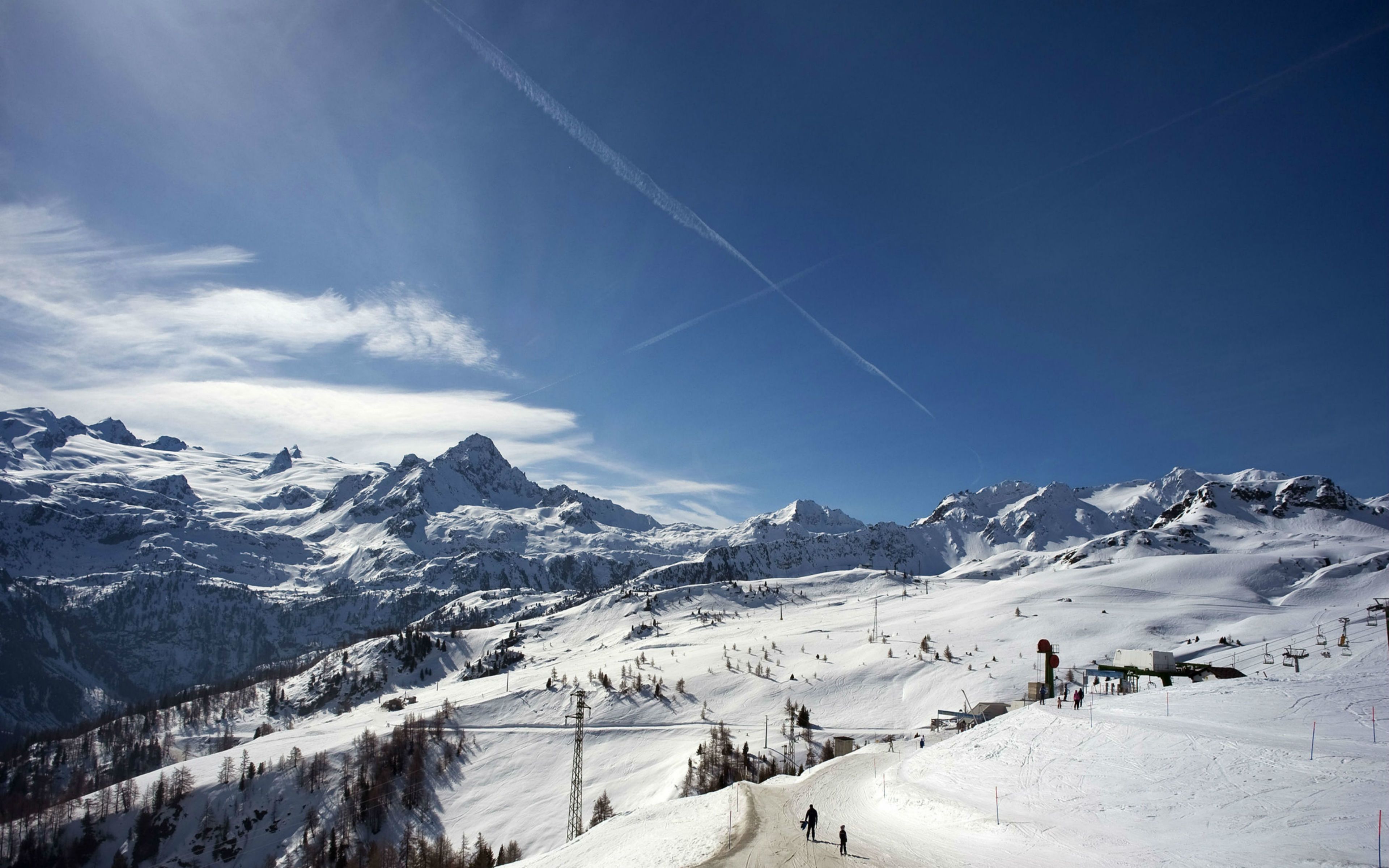 Een berglandschap bedekt met sneeuw, met skipistes, skiliften en een heldere lucht.