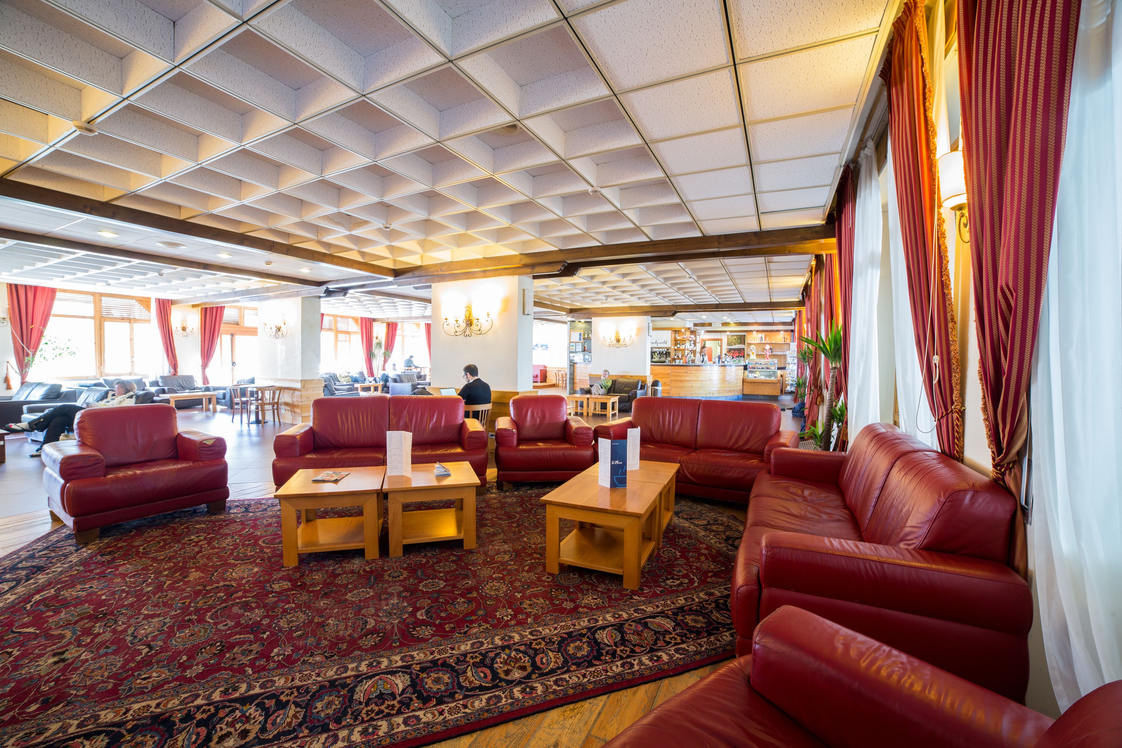A spacious lobby with red leather sofas, wooden coffee tables, and a patterned carpet.