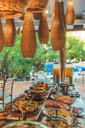 A buffet table with various food items and a pool in the background. - Cala Luna Boutique Hotel & Villas (Tamarindo)