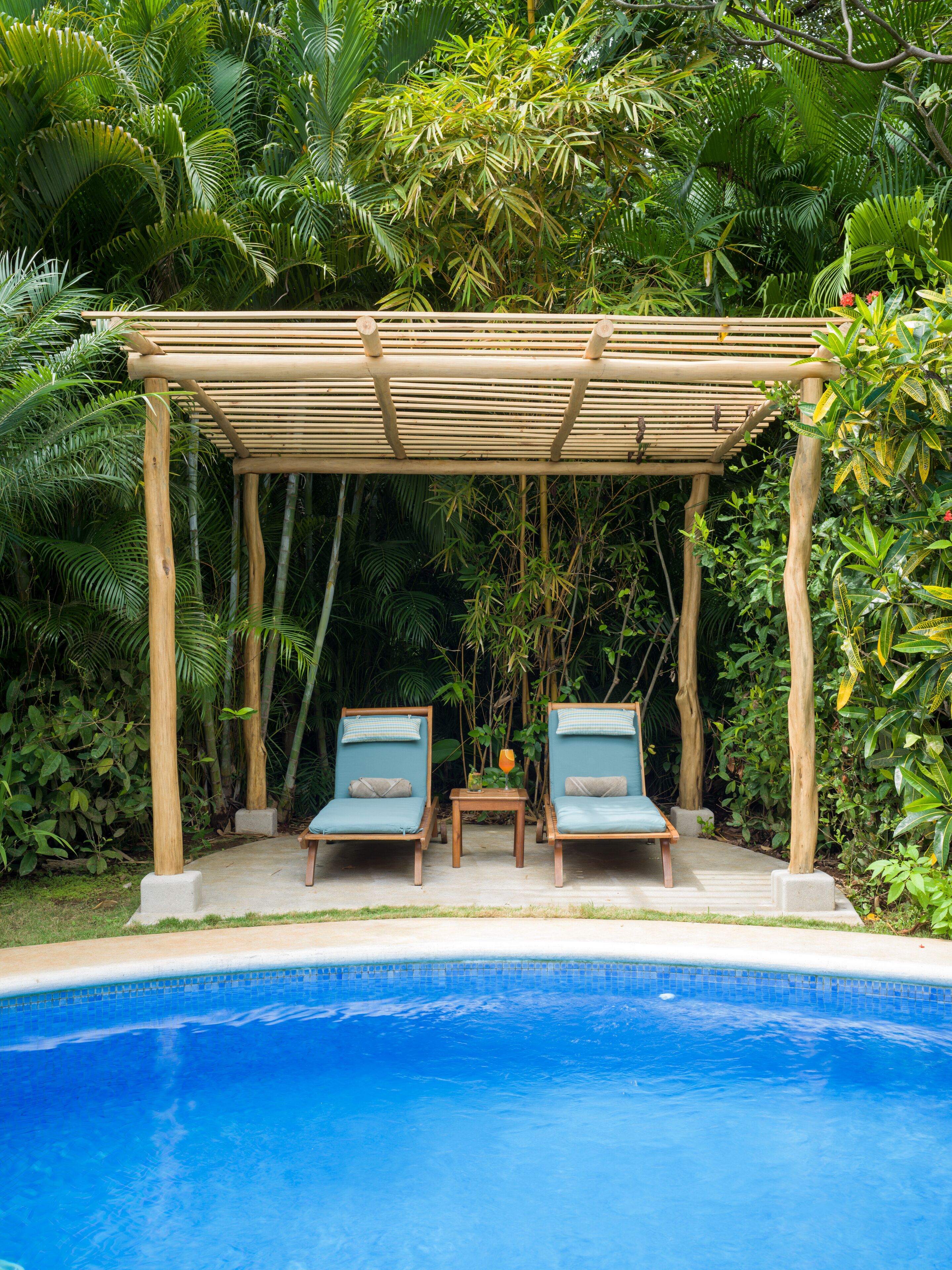 Un espace aménagé au bord de la piscine, avec une pergola en bois, deux chaises longues et une petite table sur laquelle est posé un vase.
