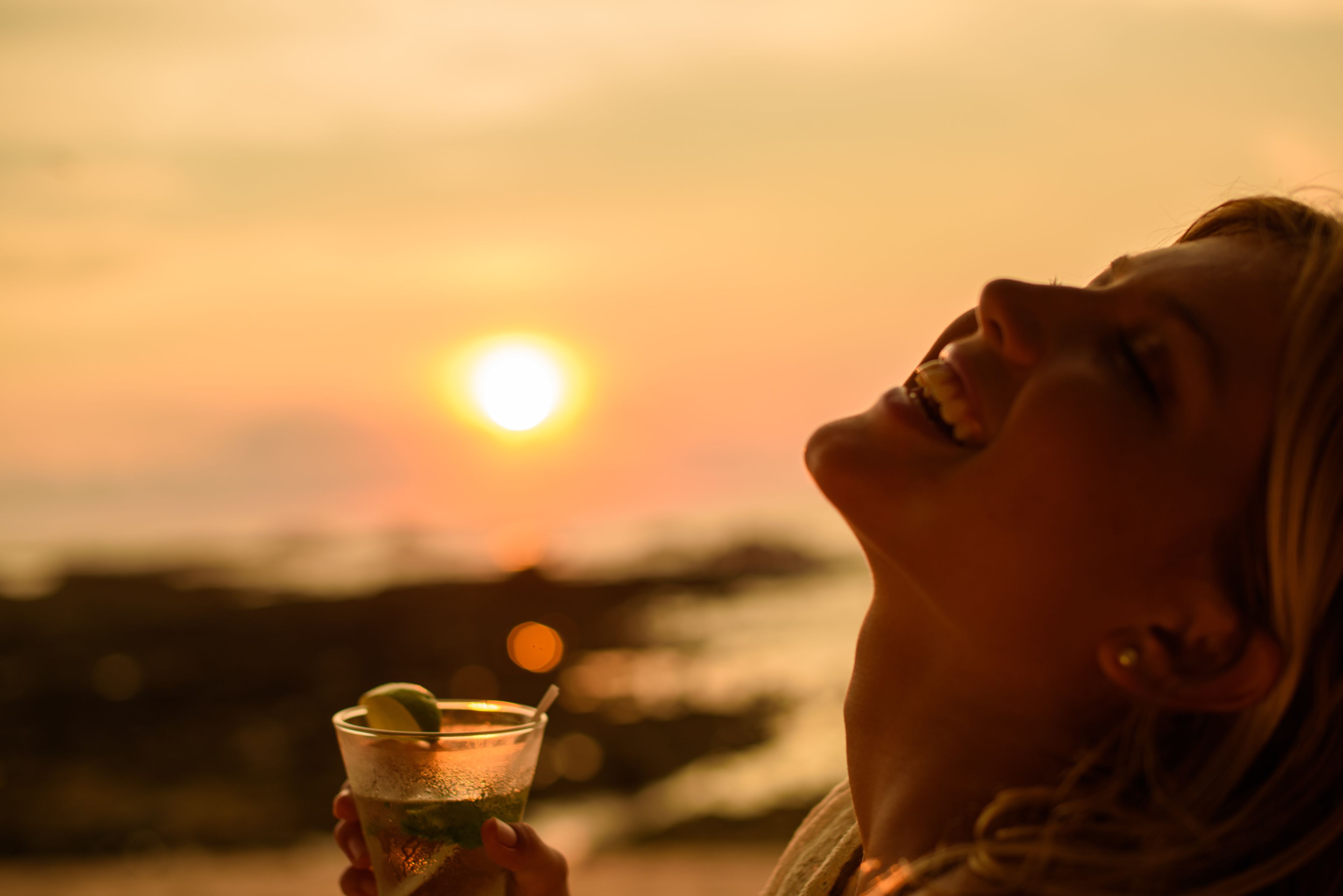Una persona sosteniendo un vaso con una bebida, con un atardecer de fondo.