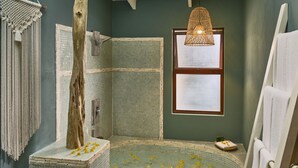 A bathroom with a bathtub, a shower, a hanging light fixture, and a window.