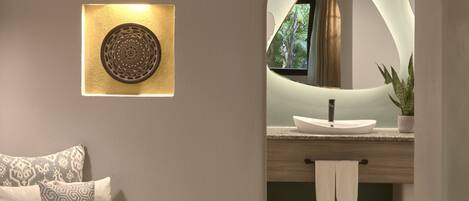 A modern bathroom with a vanity, a sink, and a mirror. There is a towel hanging on the wall and a plant on the counter.