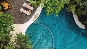 Vista aérea de un resort con una gran piscina rodeada de áreas de descanso y plantas tropicales.